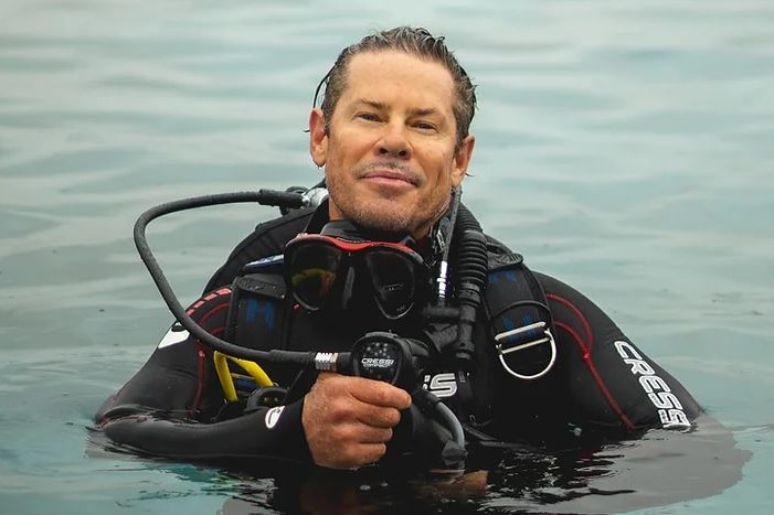 Scuba diver with head out of water looks at camera.