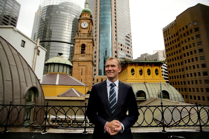 Rob Stokes, in suit and tie, stands on the roof of a building surrounded by the Sydney CBD.