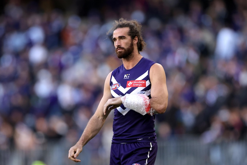 A Fremantle Dockers AFL player walks off teh ground with his arm wrapped in ice.