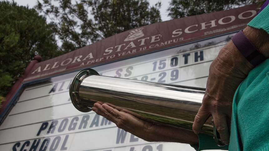 Hands hold a silver time capsule in front of a school sign