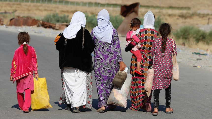 Women and children from the minority Yazidi sect walk along dusty road