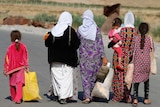 Women and children from the minority Yazidi sect walk along dusty road