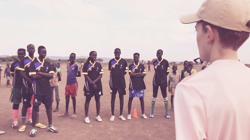 A young boy from Australia called Conrad speaks to a line of boys and girls at a Kenyan soccer training exercise.
