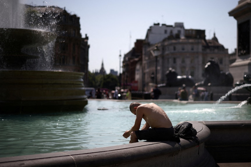 Un hombre sentado al borde de una fuente inclinado hacia adelante, parece derrotado por el calor.