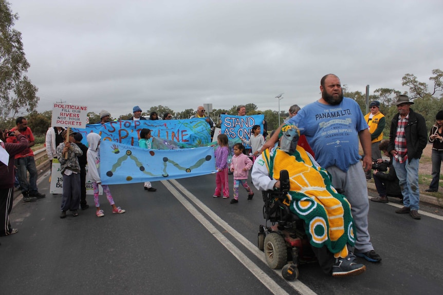 Residents of Wilcannia stand on the bridge over the Darling River, blocking cars and holding signs in protest