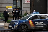 Police officers stand outside Spain's Ministry of Defence, with police car parked on curb.