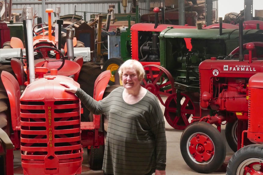 A woman stands in a large shed surrounded by many vintage tractors
