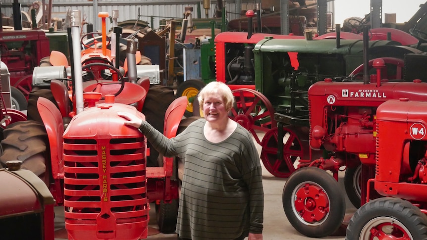 A woman stands in a large shed surrounded by many vintage tractors