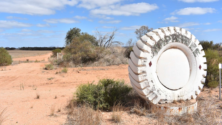 Large white painted tractor tyre with ' Napandee' name appearing across the top in faded green tape