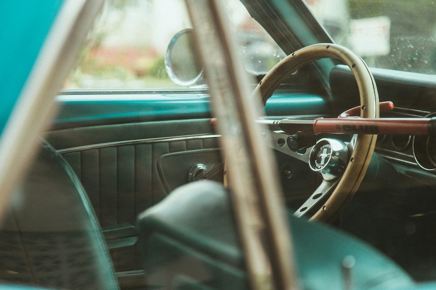 A view inside the window of a sky blue, classic car, showing a red metal bar lock device on the steering wheel.