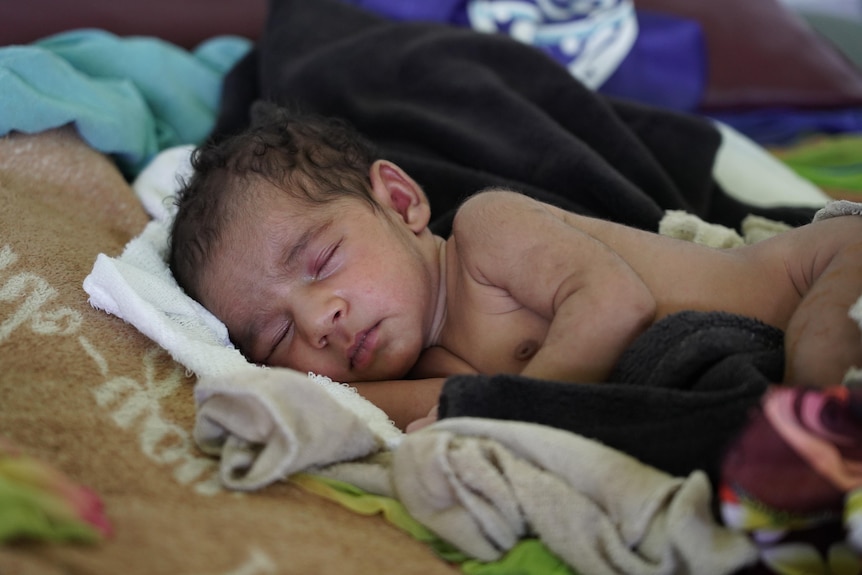 A little naked baby sleeps on a bed of assorted clothes and towels