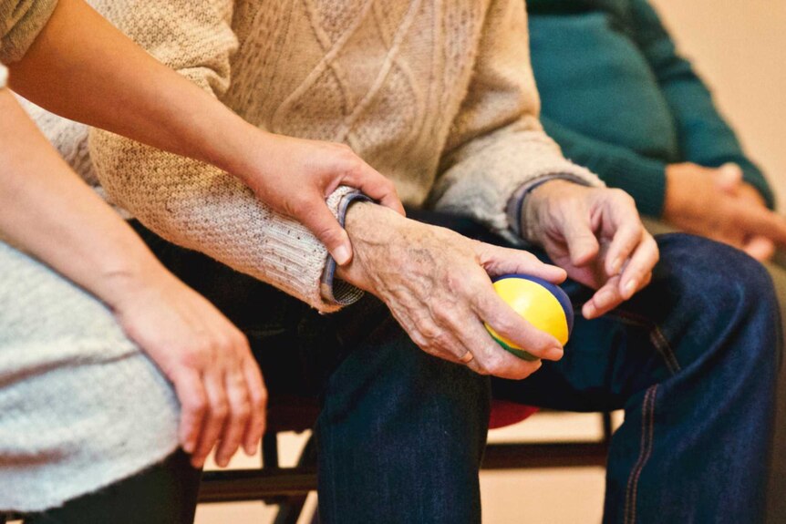 Hand of an elderly person squeezing a stress ball while being comforted by someone to depict the stress of the ICU on visitors.