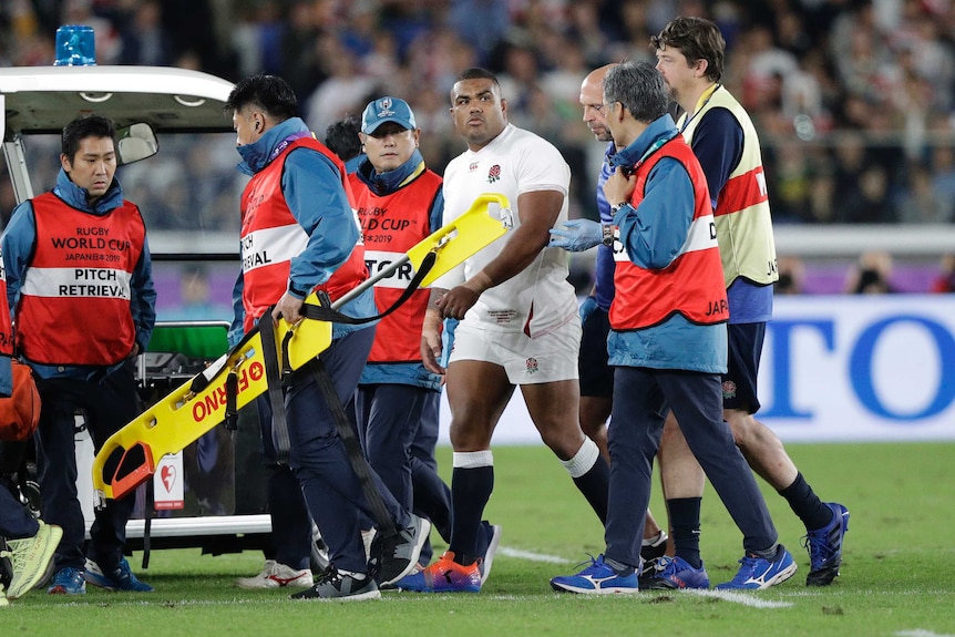 An England player looks to his left as he is led off the field by medical officials in the Rugby World Cup against South Africa.