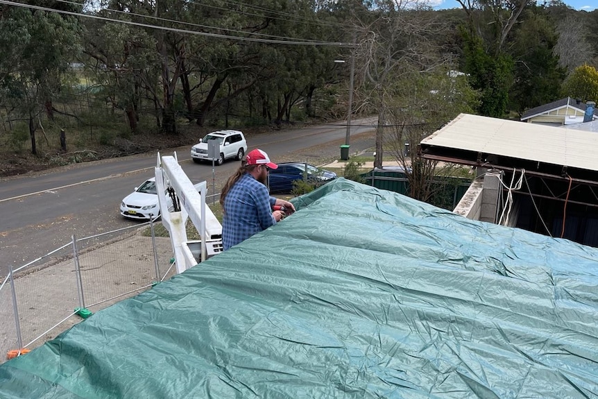 Man on a mechanical lift attached a tarp to a roof
