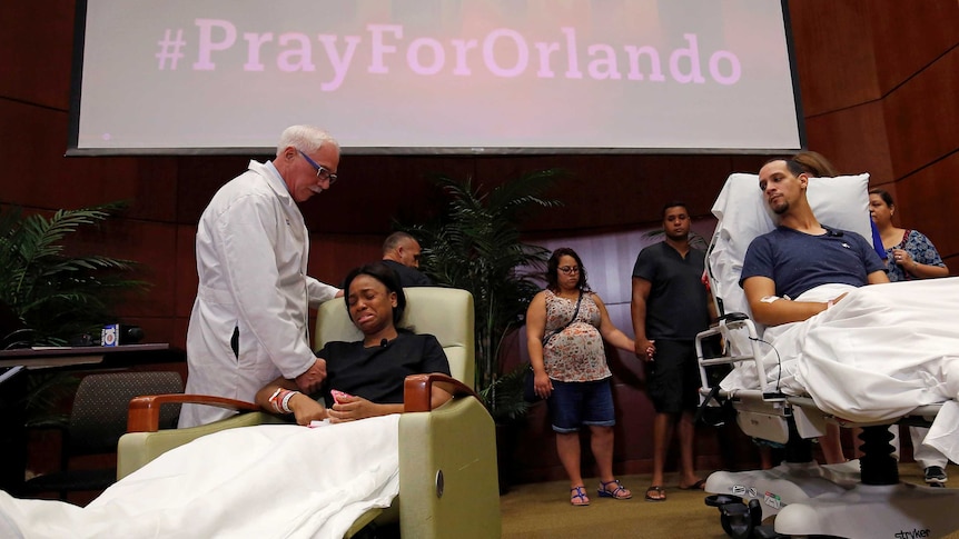 A doctor touches the shoulder of a woman sitting in a hospital chair crying. A man in a hospital bed watches on.