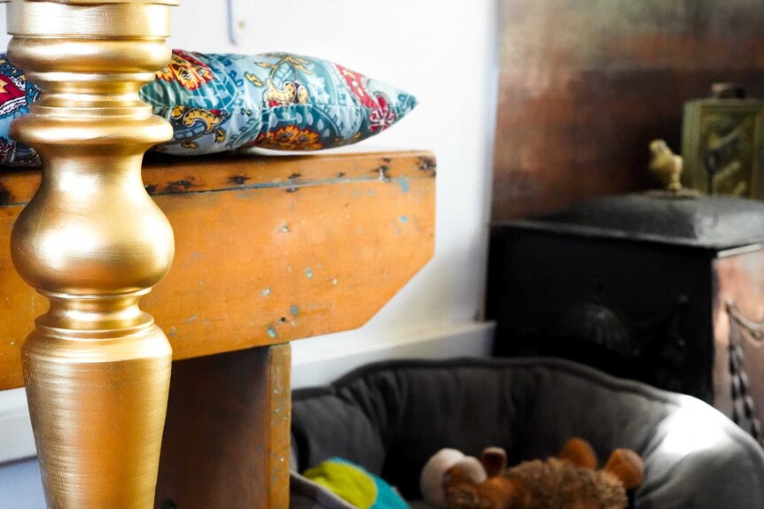 A bright gold-painted table leg stands out among a backdrop of coloured cushions and an old gas stove in the converted bus.