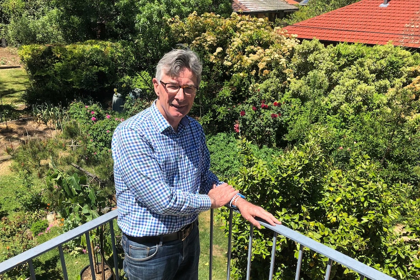 Adrian van Leest, who grows tomatoes in his large veggie patch, or hobby farm. He is on a balcony with his lush garden behind.