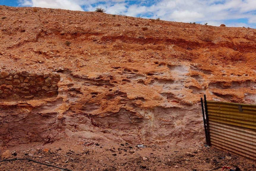 A corrugated iron fence meets a large wall of red rocks.