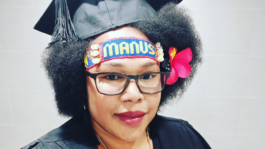 Sophie Sindra Hepota smiling, wearing black glasses, Manus bilas headband, flower in hair, graduation cap on. 