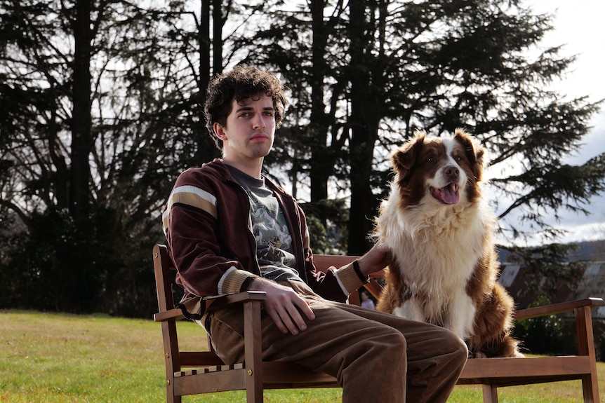 A man sits on a park bench next to a dog.
