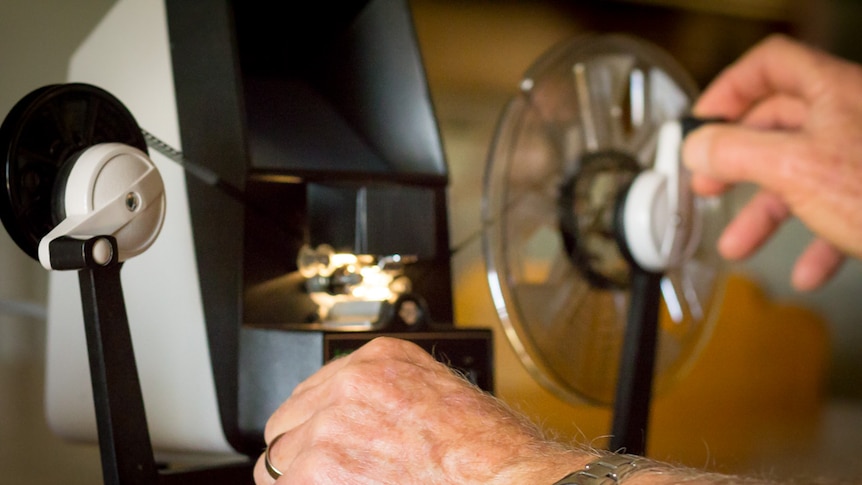 Close up of Ken Morley's hands as he feeds a reel of film through a reel to reel viewer