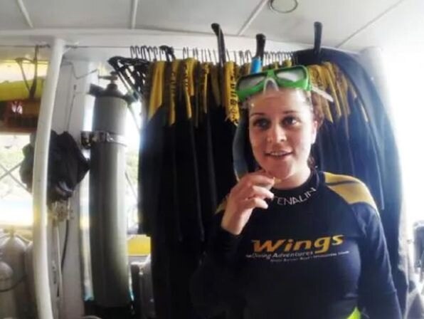 Young woman in diving gear with diving equipment behind her.
