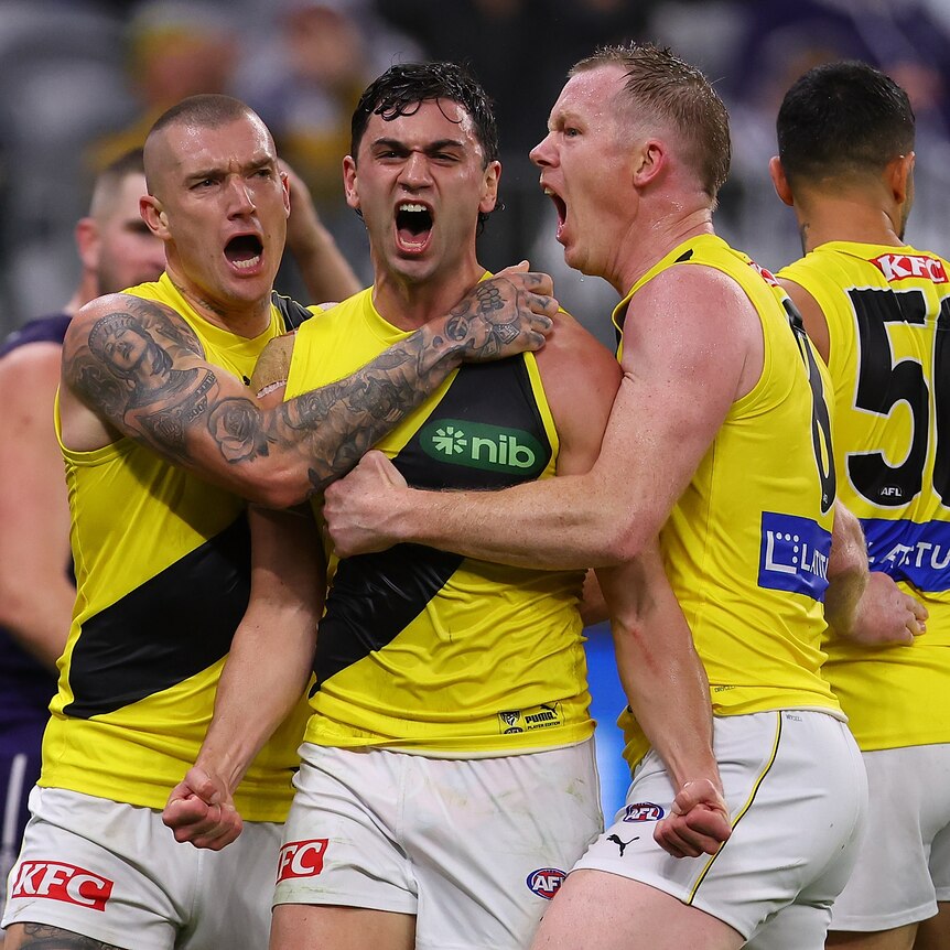 Three Richmond AFL players shout in celebration after a goal.