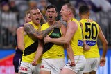 Three Richmond AFL players shout in celebration after a goal.