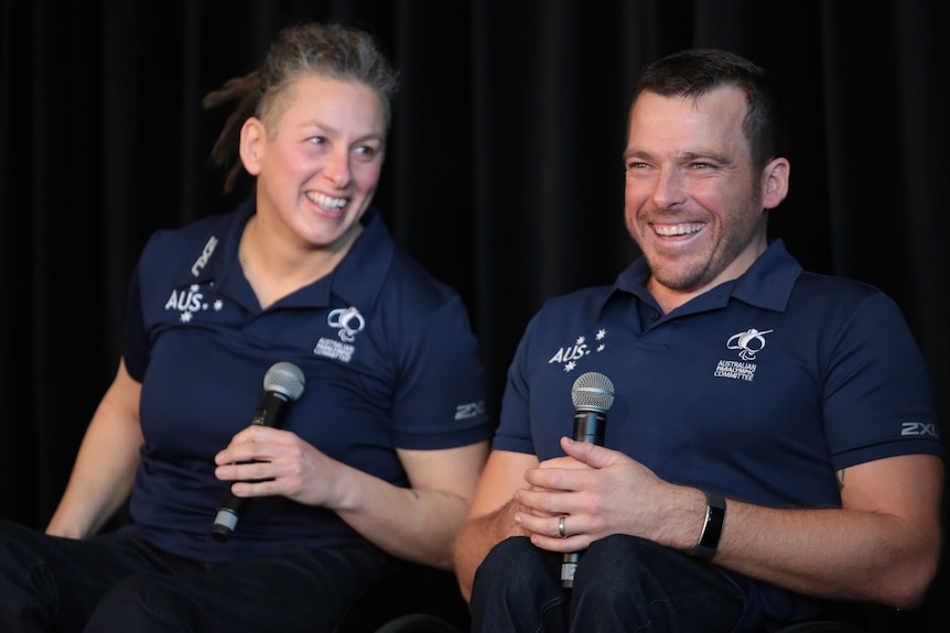 Two Australian Paralympians sit side by side at a press conference, laughing as they hold microphones.