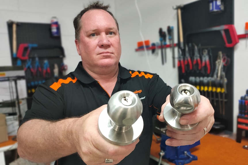 A man in a branded polo shirt holds up two doorknobs that have been damaged.