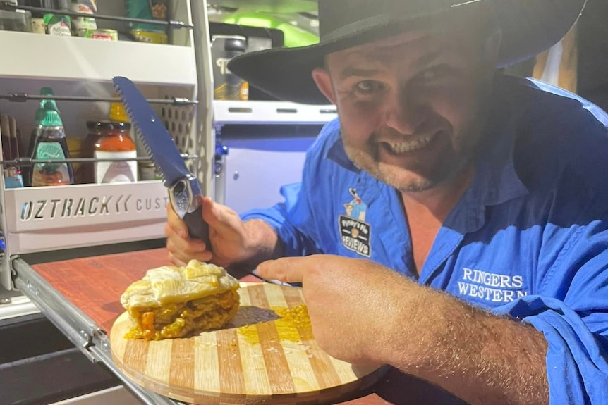 A man in a wide-brimmed hat smiles while sitting down to eat a pie