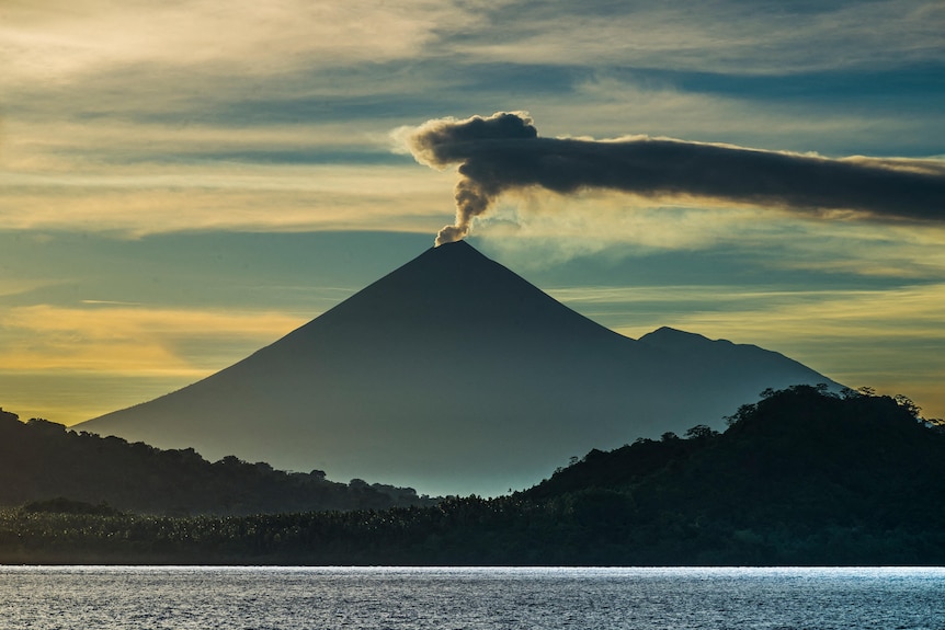 Smoke rising from the volcano against a blue sky.
