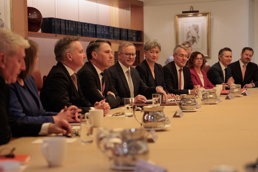 Men and women in suits sit around a curved table in an office.