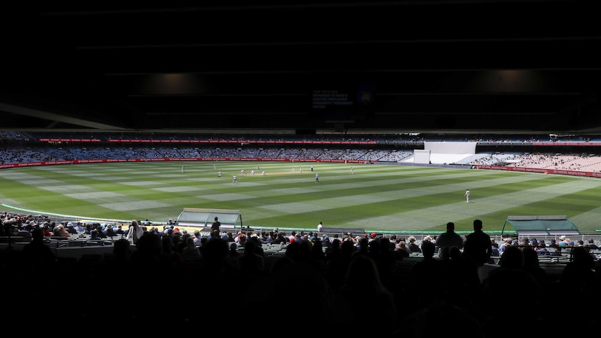 A view of the Melbourne Cricket Ground from under one of the grandstands, with fans in foreground.
