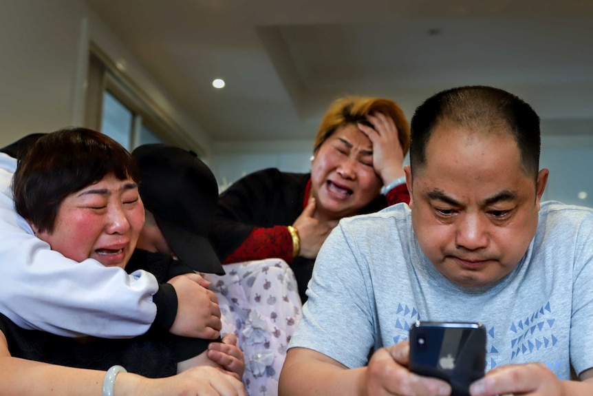 Dillon Wu's mother, sister, and aunt cry at the dining room table, while Dillon's father stares at his phone.