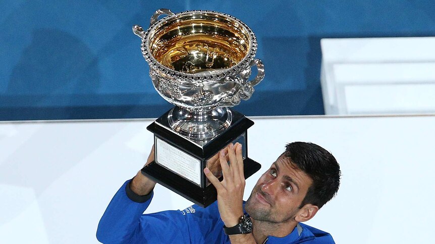 Novak Djokovic holds up Australian Open trophy on the podium