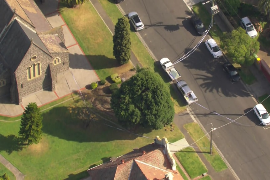 An aerial shot shows police tape running from a church to a pole and from cars parked beside the church across a street.