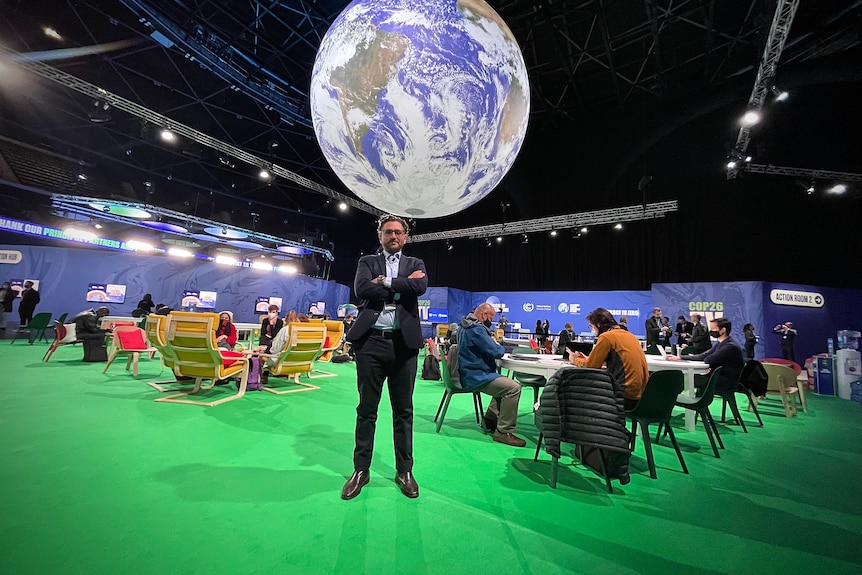 一个西装革履的男人站在会议中心的一个大地球仪前。