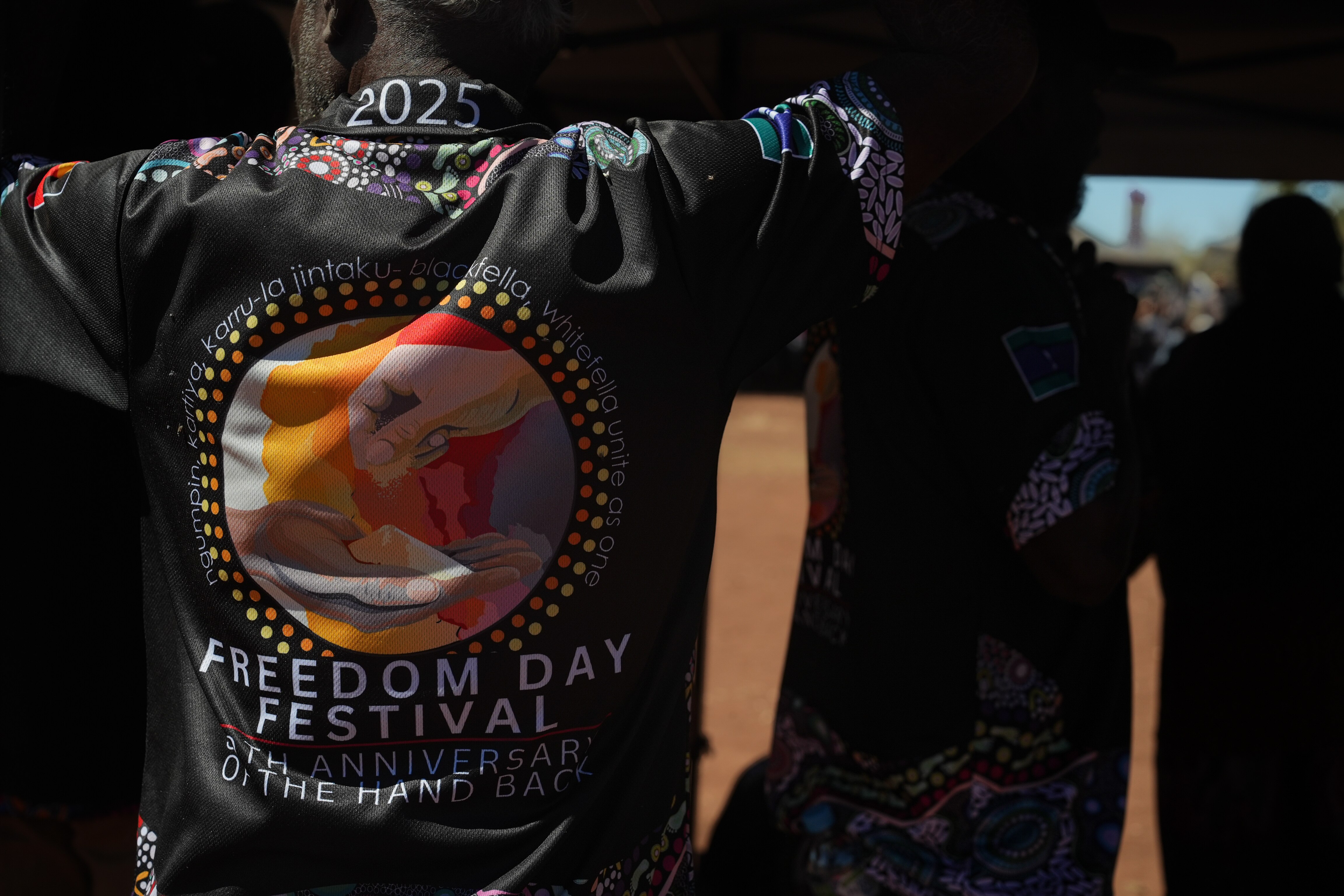 An Indigenous person wears a shirt that reads: 2025 Freedom Day festival, 50th anniversary of the hand back.