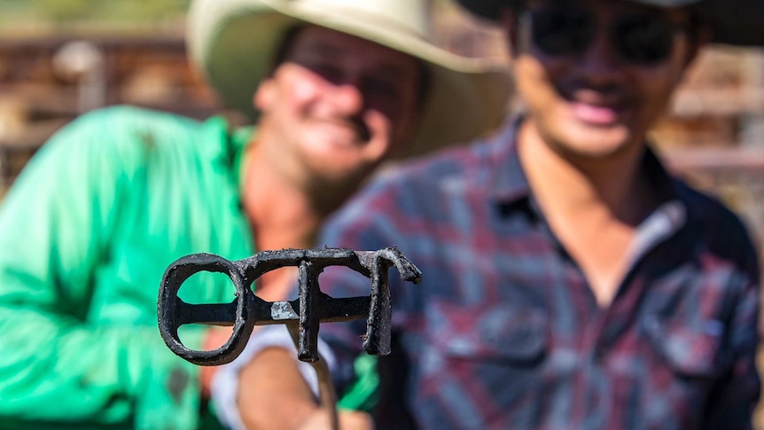 Two men holding up a branding iron