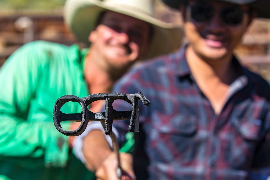 Two men holding up a branding iron