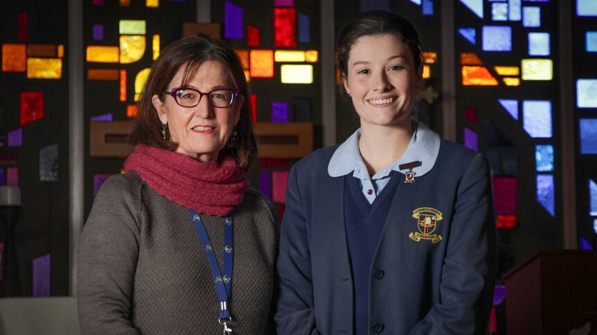 Two woman standing in front of a stained glass window inside a school chapel.