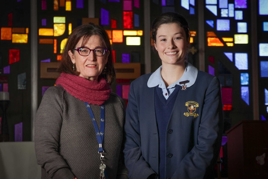 Two woman standing in front of a stained glass window inside a school chapel.