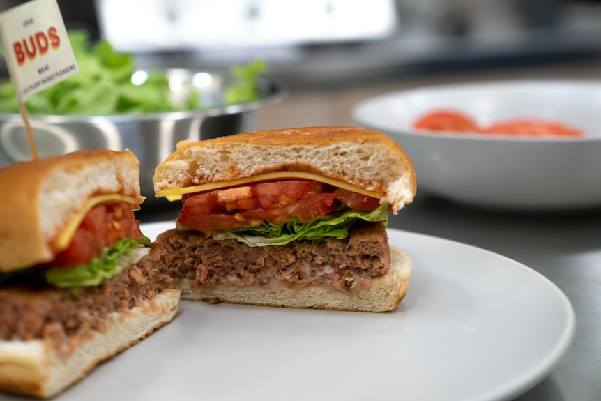 A plant-based burger is sliced in half on a plate.
