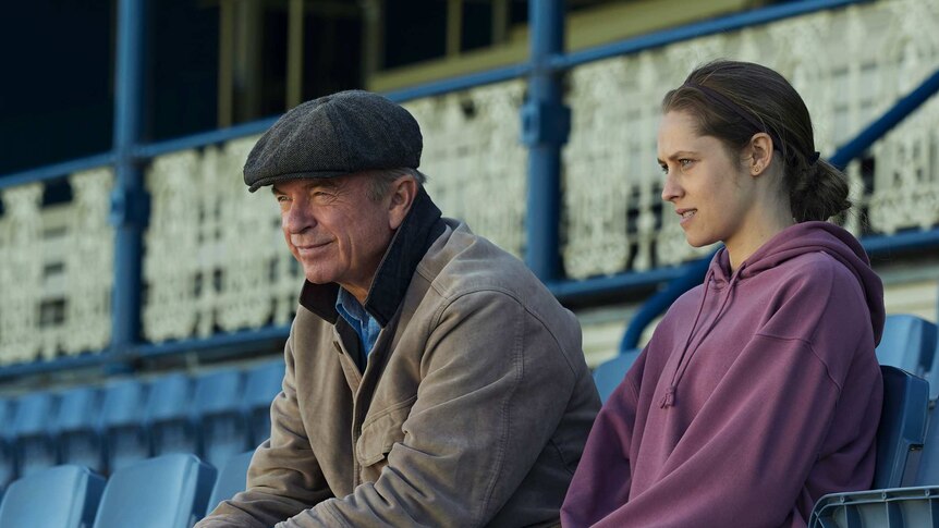 A father and daughter sit in the grandstand by themselves at a racetrack.