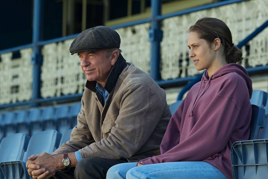 A father and daughter sit in the grandstand by themselves at a racetrack.