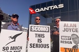 Three men hold signs protesting Qantas outsourcing, in front of the Qantas headquarters building.