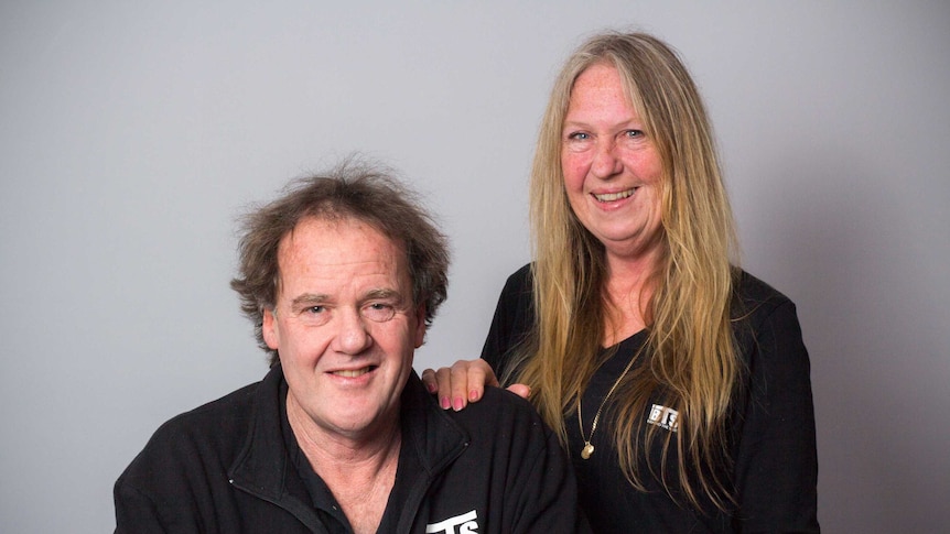 Ross Beckley and Veronique Moseley stand in front of a grey wall.