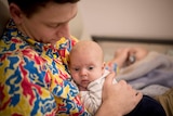A man with a colourful shirt sitting on a couch with a baby