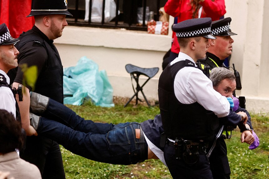 A man being carried by his legs and arms by police
